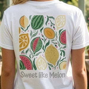 Könnte beinhalten: Weißes T-Shirt mit einem farbenfrohen Fruchtdesign auf dem Rücken, darunter Wassermelone, Zitronen und Cantaloupe. Der Text "Sweet like Melon" ist unter dem Design aufgedruckt. Das Shirt besteht aus einem weichen Material.