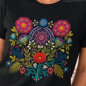 May include: A black short-sleeved t-shirt featuring a vibrant, symmetrical floral embroidery design on the chest. The pattern includes large pink and orange flowers, a central purple mandala-like bloom, red poppies, blue cacti, and small pomegranates.