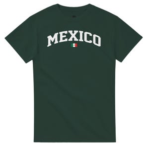Puede incluir: Camiseta verde oscuro con la palabra "MEXICO" en blanco, arqueada sobre el pecho. Un peque&ntilde;o gr&aacute;fico de la bandera mexicana est&aacute; centrado debajo del texto. La camiseta tiene mangas cortas y cuello redondo.