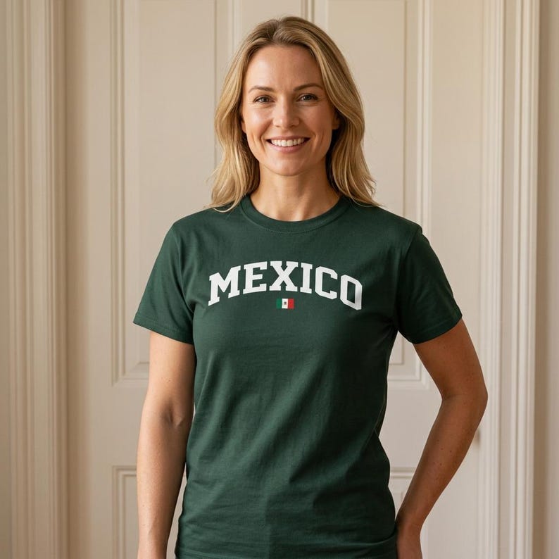 Puede incluir: Una camiseta verde oscuro con la palabra "MEXICO" en letras blancas en el pecho. Una peque&ntilde;a bandera mexicana est&aacute; colocada debajo de la palabra. La camiseta es de cuello redondo.