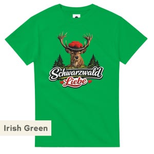 May include: An Irish green short-sleeve t-shirt featuring a graphic of a deer wearing a traditional Bollenhut hat. Below the deer are pine trees, a small house, and the text Schwarzwald Liebe with two small red hearts on either side of the word Liebe.