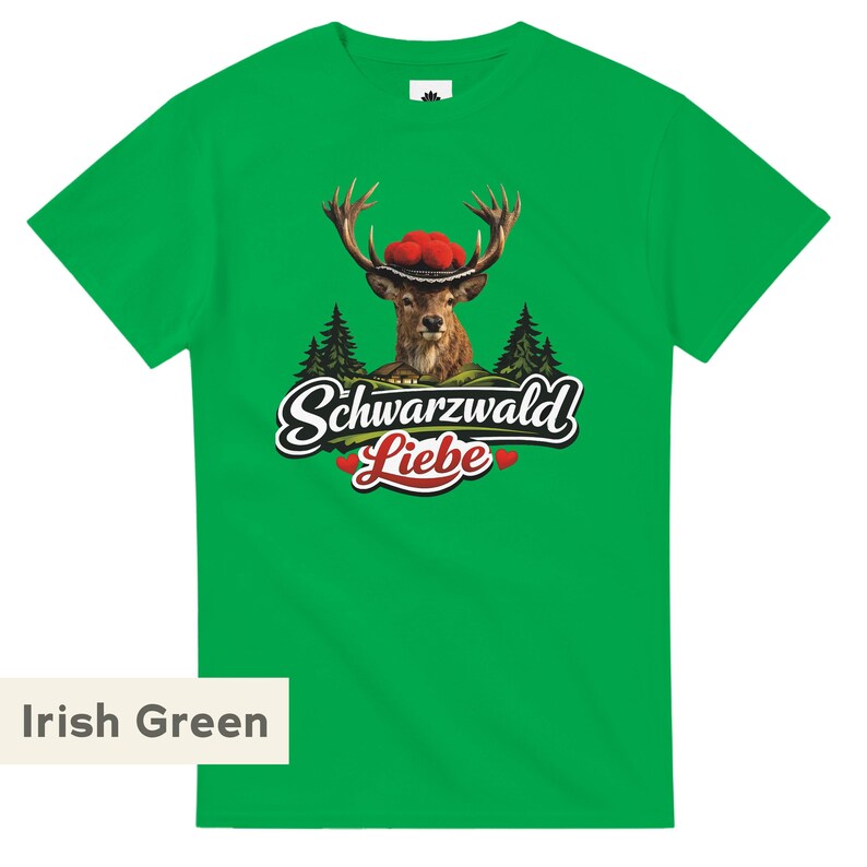 May include: An Irish green short-sleeve t-shirt featuring a graphic of a deer wearing a traditional Bollenhut hat. Below the deer are pine trees, a small house, and the text Schwarzwald Liebe with two small red hearts on either side of the word Liebe.
