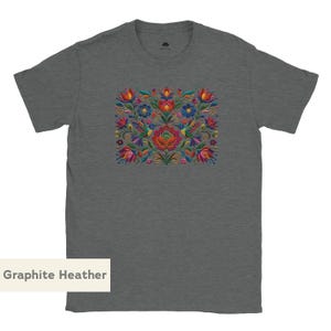May include: A graphite heather gray short-sleeve t-shirt featuring a central rectangular graphic print. The design displays a symmetrical arrangement of colorful flowers, swirling green vines, and two hummingbirds in shades of red, blue, and yellow.