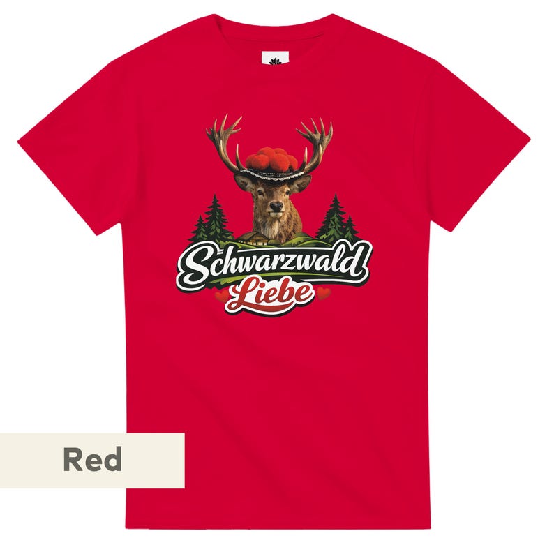 May include: A bright red short-sleeved t-shirt featuring a graphic of a deer wearing a traditional red pom-pom hat. Below the deer are green pine trees and the text Schwarzwald Liebe in a white script font with a black outline and red hearts.