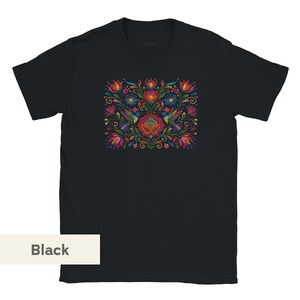 May include: A black short-sleeve t-shirt featuring a central graphic print of colorful hummingbirds surrounded by vibrant red, blue, orange, and green floral patterns and swirling vine motifs arranged in a symmetrical, dense botanical composition.