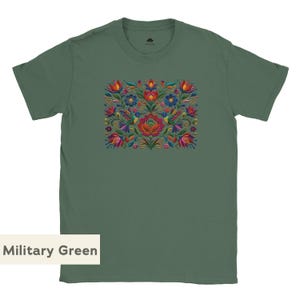 May include: A military green short-sleeve t-shirt featuring a central rectangular graphic print of colorful flowers, leaves, and two hummingbirds in shades of red, blue, yellow, and pink. The shirt has a crew neckline and a small logo on the inner neck.