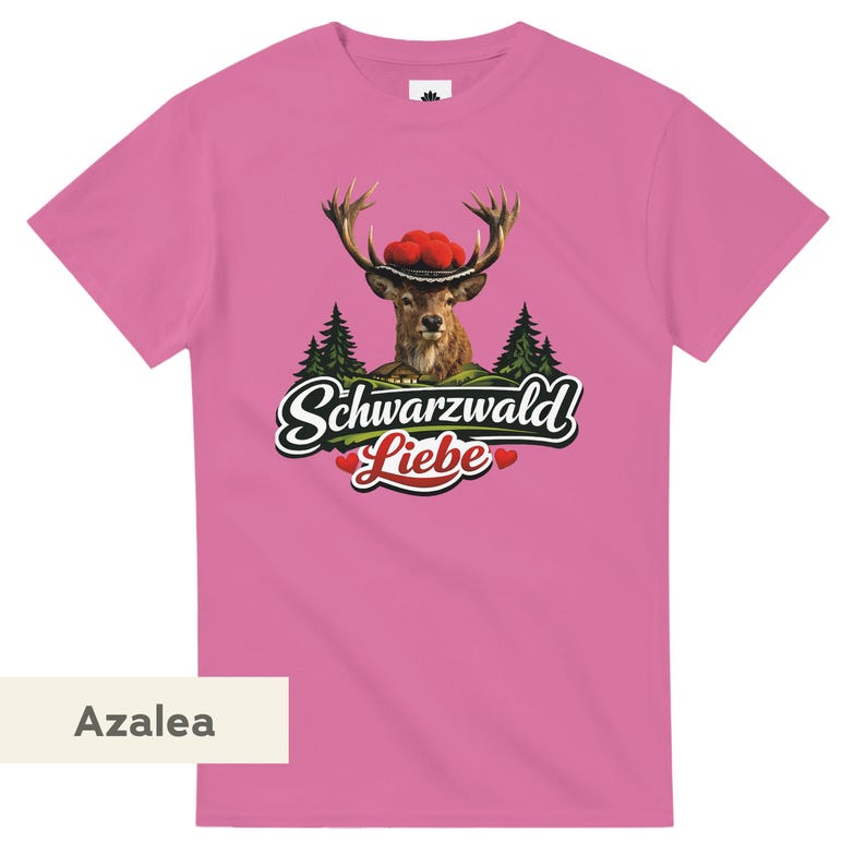 May include: A pink short-sleeved t-shirt featuring a graphic of a deer wearing a red pom-pom hat. Below the deer are green pine trees and the text Schwarzwald Liebe with two small red hearts. The shirt is labeled with the color name Azalea.