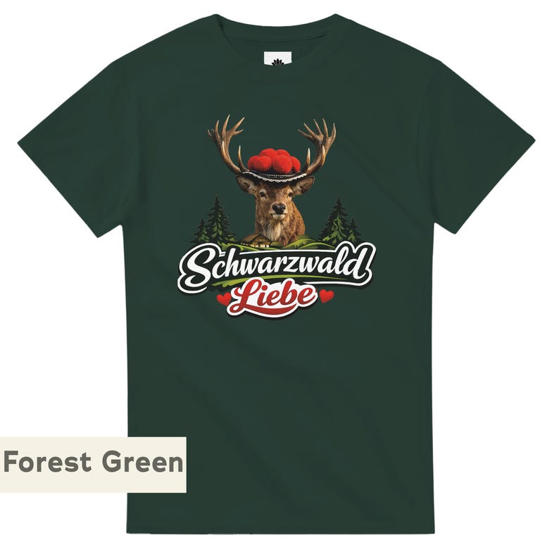 May include: A forest green short-sleeve t-shirt featuring a graphic of a deer wearing a traditional red pom-pom hat. Below the deer are green pine trees and the white text "Schwarzwald" above the red text "Liebe" with two small red hearts.