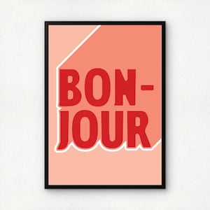 Puede incluir: Una impresión artística enmarcada con la palabra "BONJOUR" en letras rojas en negrita. La palabra está sobre un fondo color melocotón con un acento blanco y coral. El marco es negro.