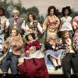 May include: A collection of miniature dolls dressed in various outfits. The dolls are of different genders and ethnicities, and are wearing clothing such as jackets, dresses, and robes. The dolls are arranged in a group, suggesting a family or community.