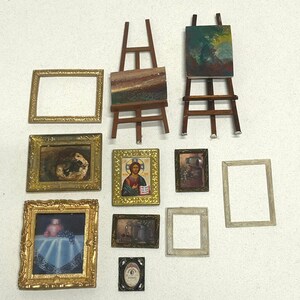 Puede incluir: Una colección de pinturas en miniatura enmarcadas y caballetes de arte. Las pinturas presentan varios estilos, incluyendo paisajes, retratos y arte abstracto. Los marcos son dorados y ornamentados, con una variedad de formas y tamaños. Los caballetes son de madera y sostienen pequeños lienzos.