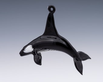 May include: Black glass ornament of an orca whale with a white patch on its eye, hanging from a loop.