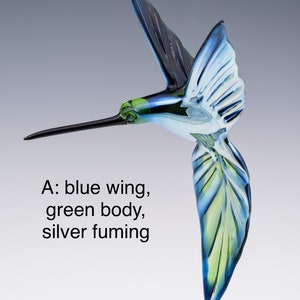 May include: A glass hummingbird sculpture with blue wings, a green body, and silver fuming. The hummingbird is in flight with its beak extended.