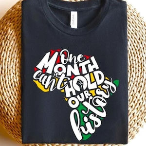 Può includere: T-shirt nero con una grafica del continente africano in rosso, giallo e verde, e la scritta "One month can't hold our history" in bianco. La maglietta è realizzata in un materiale morbido.