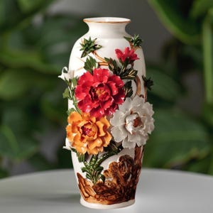 May include: White ceramic vase with a raised floral design. The vase features red, orange, and white flowers with green leaves and brown accents. The vase has a gold rim and a slightly flared shape, suitable for home decor.