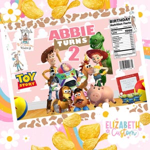 Puede incluir: Una bolsa de patatas fritas rosa personalizada con personajes de Toy Story, el texto "ABBIE TURNS 2" y una etiqueta de "Birthday Nutrition Facts". La bolsa est&aacute; decorada con patatas fritas y detalles florales.