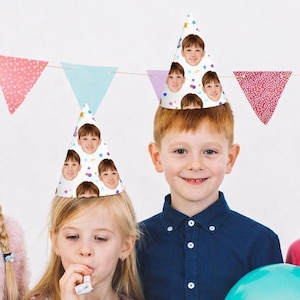 May include: Three cone-shaped party hats featuring a repeating pattern of a person's face and colourful confetti dots. The hats are white with a pointed top and are displayed above a string of triangular pennant flags in various colours.