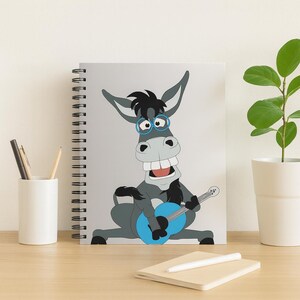 Op de afbeelding: Een spiraalgebonden notitieboek met een cartoon ezel die een blauwe gitaar bespeelt. De ezel is grijs met zwart haar en draagt een blauwe bril. De ezel heeft een grote glimlach en zit.