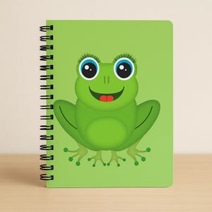 Peut inclure: Un cahier à spirales vert avec une illustration de grenouille de dessin animé. La grenouille a de grands yeux bleus avec de longs cils, une langue rouge et une expression souriante. La couverture du cahier est de couleur vert clair uni.