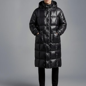 May include: A long, black puffer coat with a hood. The coat is quilted in a rectangular pattern and has pockets. The person is wearing black trousers. The coat is a winter outerwear garment.