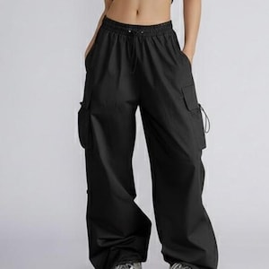May include: Black cargo trousers with a drawstring waist and multiple pockets. The trousers have a relaxed fit and are paired with grey trainers. The overall style is casual and modern.