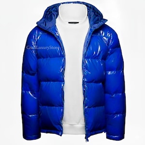 Könnte beinhalten: Glänzende, leuchtend blaue Pufferjacke mit Kapuze, getragen über einem weißen Sweatshirt. Die Jacke ist mit einem Reißverschluss versehen und hat ein gestepptes Design. Der Markenname "CraftLuxuryStore" ist auf der linken Seite der Jacke sichtbar. Oberbekleidung.