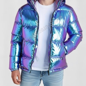 Op de afbeelding: Iridescent pufferjack met een capuchon en een ritssluiting. De kleur van de jas verschuift tussen blauw, paars en groen. De tekst "Craftxury Store" is zichtbaar op de jas. Het model draagt een wit t-shirt en een blauwe jeans.