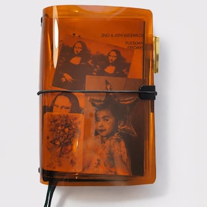 May include: An orange-tinted, rectangular case with a black elastic band and a gold-coloured clasp. Inside are several printed images, including portraits and a child's photo. Text on the top reads "2ND & 4TH WEEKS" and "TUESDAY FRIDAYS".