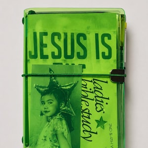 Op de afbeelding: Een fel limoengroene, doorschijnende plastic notitieboekhoes met de tekst JESUS IS en een kleinere inzet met een foto van een persoon die een stervormig hoofddeksel draagt, naast de tekst ladies bible study 2nd & 4th W.