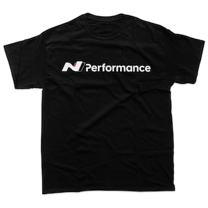 Puede incluir: Camiseta negra con el texto blanco "N Performance" y un logotipo "N" estilizado en rojo, blanco y negro. La camiseta está hecha de un material suave y tiene cuello redondo.