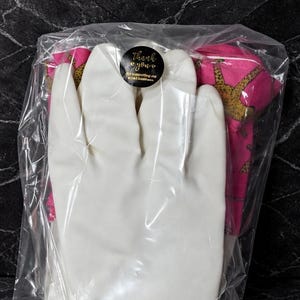 May include: A clear plastic bag containing a white glove and a pink fabric item with a gold pattern. A black sticker with gold text that says "Thank you" is visible on the bag.
