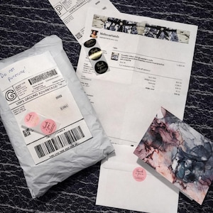 May include: An assortment of shipping materials, including a package, receipts, and a card, are arranged on a textured surface. The package is sealed with tape and includes a label with a barcode and the text "Do not puncture!".