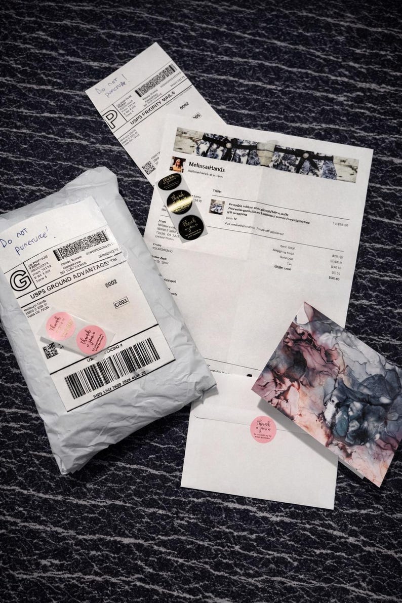 May include: An assortment of shipping materials, including a package, receipts, and a card, are arranged on a textured surface. The package is sealed with tape and includes a label with a barcode and the text "Do not puncture!".