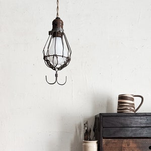 Puede incluir: Una lámpara colgante de estilo industrial con una jaula de alambre alrededor de una bombilla cuelga sobre un mueble de madera oscura. Una taza de cerámica con rayas marrones y crema está sobre el mueble.