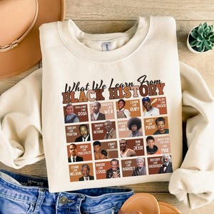 May include: Cream-colored sweatshirt with the text "What We Learn From Black History" and portraits of historical figures. The sweatshirt features a crew neck and long sleeves. The design includes portraits of Rosa Parks, Martin Luther King Jr., and others.