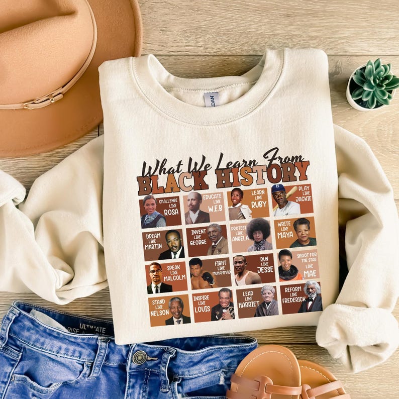 May include: Cream-colored sweatshirt with the text "What We Learn From Black History" and portraits of historical figures. The sweatshirt features a crew neck and long sleeves. The design includes portraits of Rosa Parks, Martin Luther King Jr., and others.
