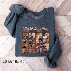 May include: Dark gray heather sweatshirt with the text "What We Learn From Black History" and portraits of historical figures. The sweatshirt features a crew neck and long sleeves. The text "DARK GRAY HEATHER" is at the bottom.