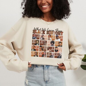 May include: Cream-colored sweatshirt with the text "What We Learn From Black History" in black and brown. The design includes portraits of historical figures like Rosa Parks, Martin Luther King Jr., and Maya Angelou. A stylish and educational apparel item.