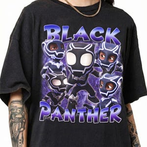 May include: A black short-sleeved t-shirt featuring a graphic print of five stylized Black Panther characters in masks. The text "BLACK PANTHER" is printed in large, bold, purple-outlined letters above and below the characters on a purple nebula background.