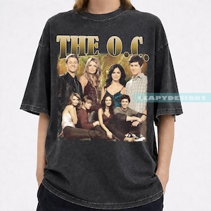 May include: Dark gray t-shirt featuring a group photo of the cast of "The O.C." in a vintage style. The text "THE O.C." is printed in gold across the top. The shirt has a worn, distressed look.