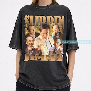 Peut inclure: T-shirt gris foncé avec un graphisme vintage d'un homme et le texte doré "Slippin' Jimmy". Le design comprend plusieurs images de l'homme dans différentes poses. Le t-shirt a un aspect usé et vieilli.