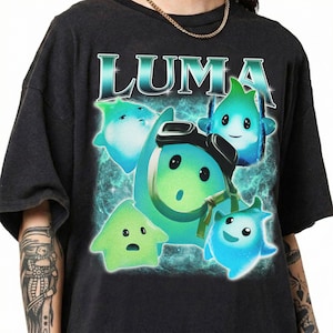 May include: A black short-sleeve t-shirt featuring a graphic print of four glowing teal and green Luma characters. The central character wears black goggles. The word LUMA is printed in large, stylized white and teal letters above the characters.
