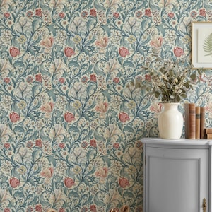 May include: Wallpaper featuring a dense floral pattern in muted blue, cream, and red tones. A light gray curved cabinet holds a white vase with dried foliage, three stacked books, and a framed fern print. A woven basket contains a white cloth.