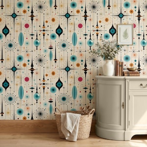 Peut inclure: Papier peint avec un motif répétitif d'étoiles et de formes géométriques noires, bleu sarcelle, roses et orange sur fond crème. Un vase blanc avec du feuillage séché, une pile de livres et un panier tressé avec un tissu blanc sont présents.