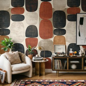 May include: A room interior featuring wallpaper with large, rounded geometric shapes in rust, charcoal, and beige. A cream-coloured armchair with a leopard print throw, a brass side table, a record player, and a patterned rug are visible.