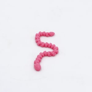 May include: A bright pink articulated snake toy. The toy is made of connected segments, allowing it to bend and move. The snake has a rounded head with small, circular eyes. The toy is set against a white background.