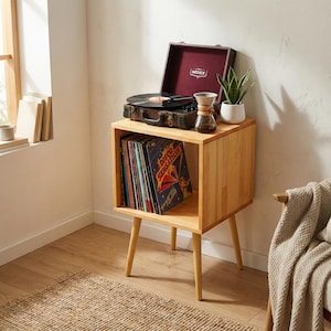 以下が含まれることがあります： レコードプレーヤー、レコード、小さな植物が置かれた明るい木製のレコードプレーヤースタンド。 レコードプレーヤーは黒色で、茶色のケースが付いています。 レコードは下のコンパートメントにあります。 スタンドには4本の脚があります。