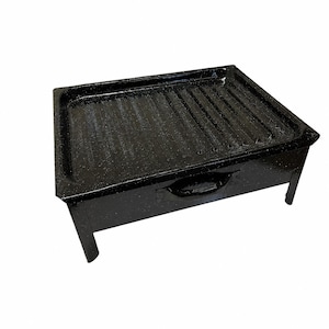 Puede incluir: Una parrilla rectangular de esmalte negro con acabado moteado, que presenta una superficie de cocción acanalada elevada para sellar alimentos. La parrilla se apoya sobre cuatro patas cortas y resistentes e incluye un asa integrada.