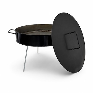 May include: A black circular cooking pan with two side handles, supported by three thin metal legs. The pan features a matching round black lid with a central handle, positioned upright next to the main body of the cooking vessel.
