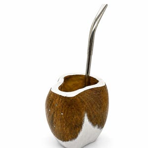 Può includere: Un contenitore per mate in legno marrone con base e bordo dipinti di bianco, caratterizzato da una venatura del legno naturale. Una cannuccia bombilla in metallo color argento, sottile e curva, è inserita nell'apertura del contenitore.
